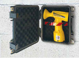 A yellow handheld device with red and black striped tape wrapped around it, displayed inside an open black hard case with foam lining against a light gray textured wall.