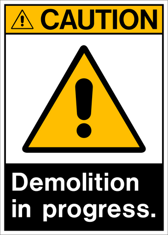 A yellow rectangular sign with black text and iconography indicating 'Demolition in Progress.'