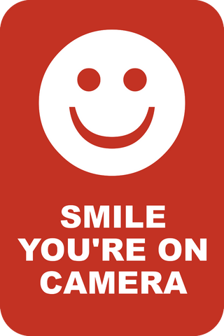 A red sign with a white smiley face and the text 'SMILE YOU'RE ON CAMERA'.
